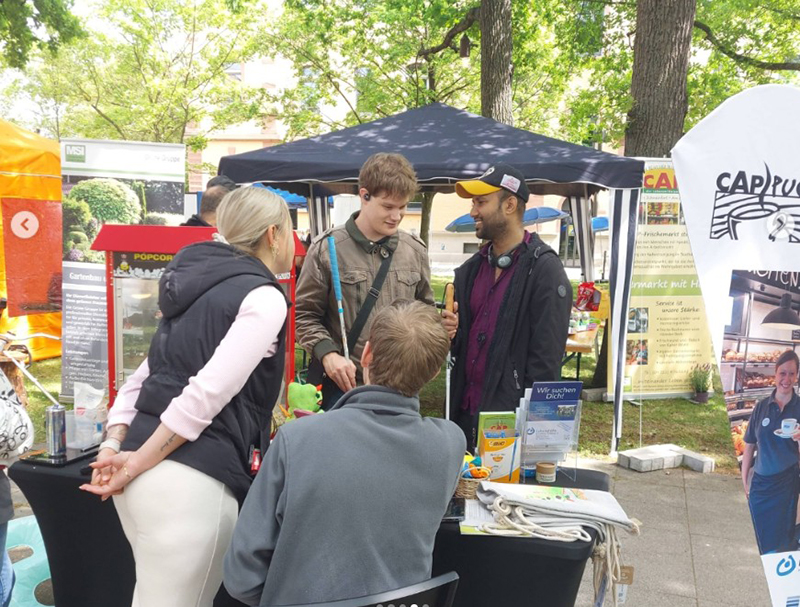 Teilnehmende im Gespräch an einem Messestand