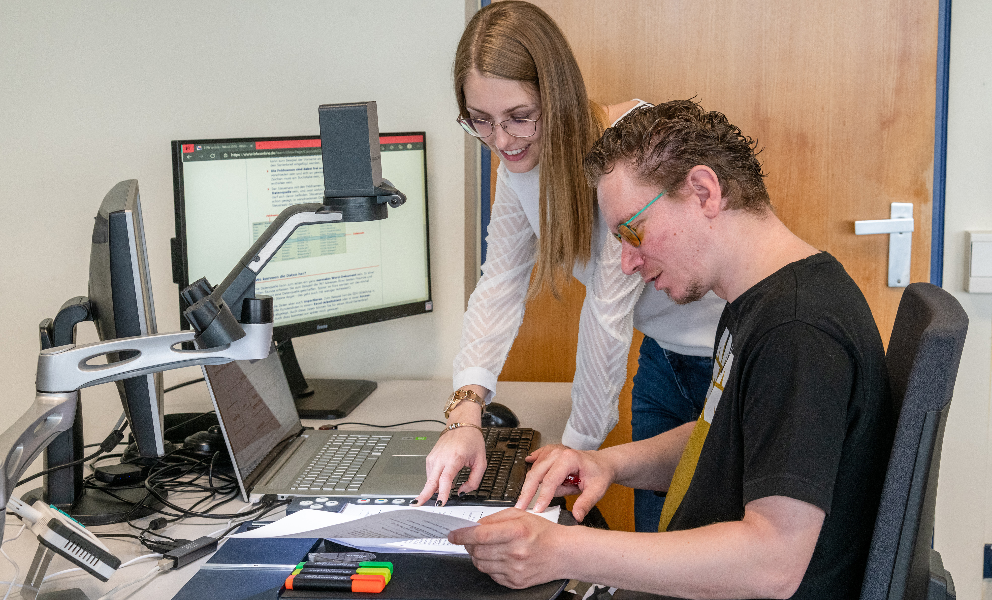 Foto eines eines Teilnehmers mit einer Ausbilderin an einem sehbehindertengerechten PC-Arbeitsplatz